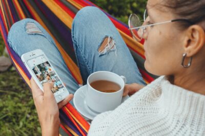 Millennial trendy blogger woman check Social media Instagram photo drink tea in hammock garden