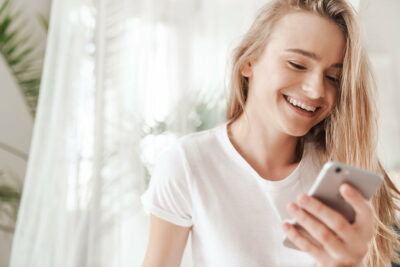 Image of nice young woman typing on smartphone and laughing