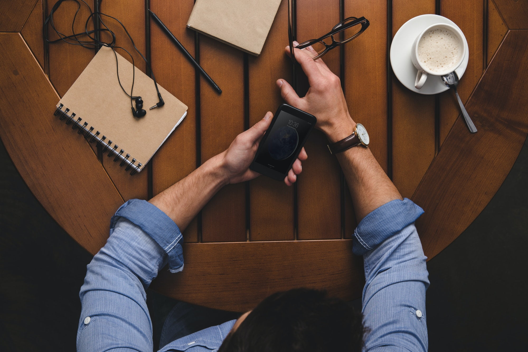 overhead view of man using iphone at wooden table with coffee and notepads