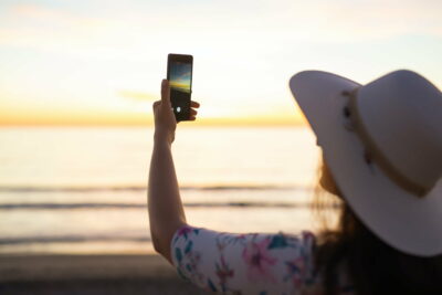 Traveler young woman is shooting video of beautiful sunset landscape on mobile phone camera. Summer