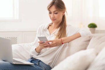 Woman Texting On Phone Working On Laptop At Home