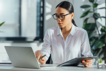 asian translator in eyeglasses working online with laptop in office