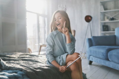 I know! Cute little girl gesturing and smiling while playing with a magic wand at home