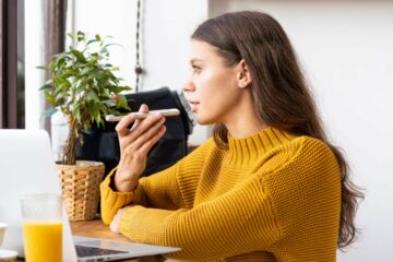 Portrait of positive young woman recording audio message, speaking to microphone