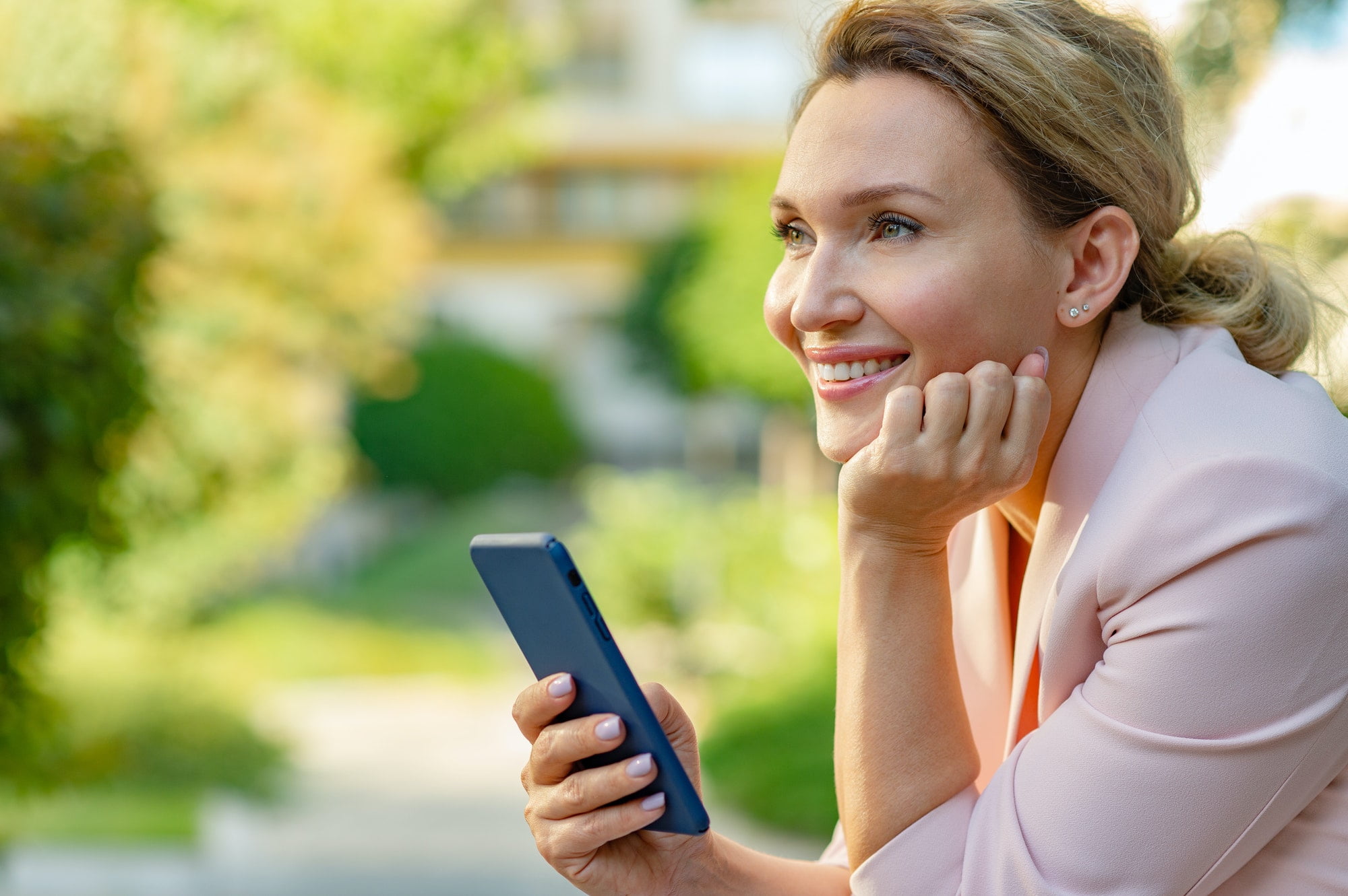 Smiling woman with smartphone on the street. Happy businesswoman is using phone, outdoors.