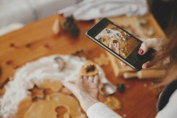 Woman holding phone and taking photo of gingerbread christmas cookies. Instagram photo