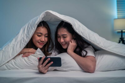 Asian attractive lesbian couple use mobile phone watch movie on bed.