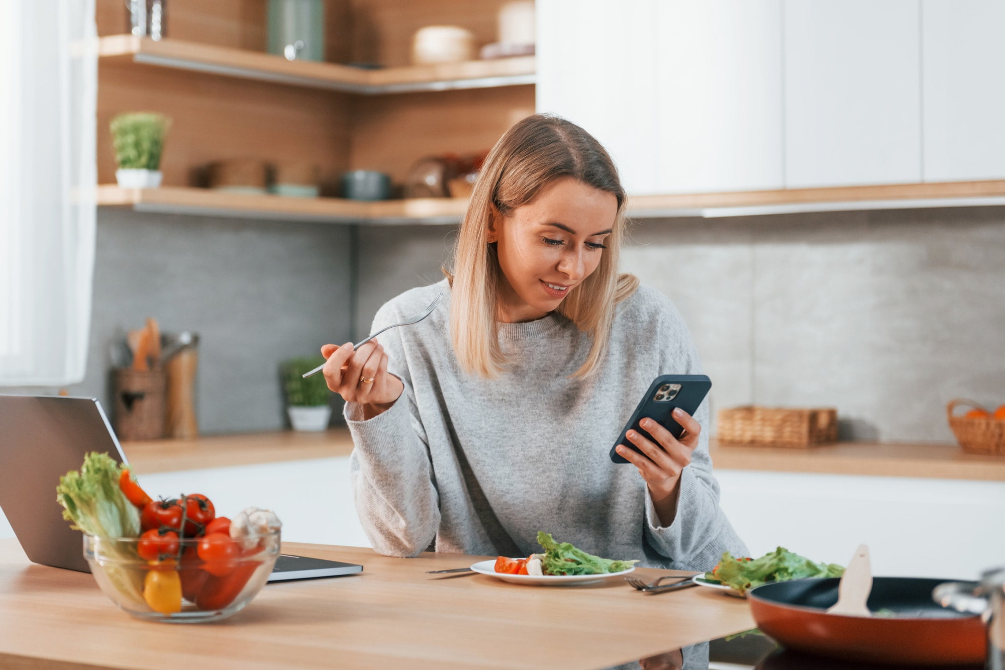 Holding phone. Woman preparing food at home on the modern kitchen