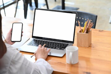 Young woman browsing websites on laptop and using mobile phone at office.