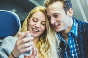 Young couple reading smartphone texts in train carriage