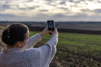 Young woman makes a photo of the field by smartphone.