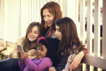 Family Using Phone While Sitting By Fence At Backyard