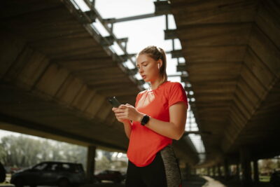 Fitness girl with headphones in her ears, plays music on phone and starts running around the city.