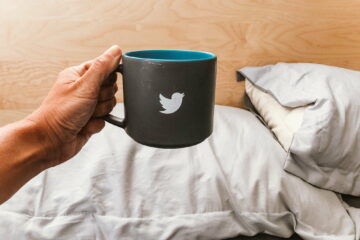 Hand holding mug with a tweeter bird sign