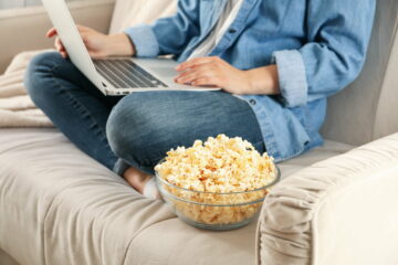 Woman watching film on sofa and eat popcorn. Food for watching films