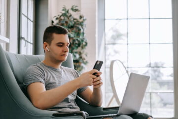 A young businessman in headphones uses a smartphone and works on a laptop