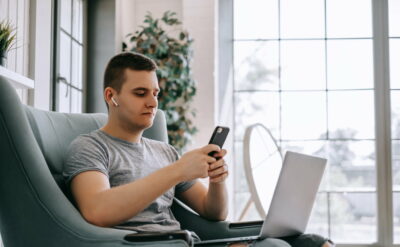 A young businessman in headphones uses a smartphone and works on a laptop