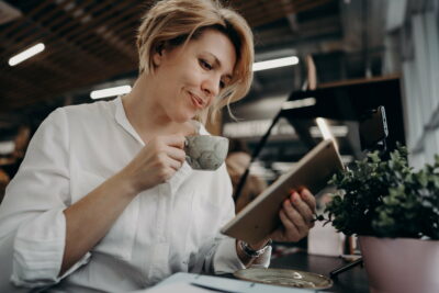 A young woman with a tablet drinks coffee, reads the news and watches videos on YouTube