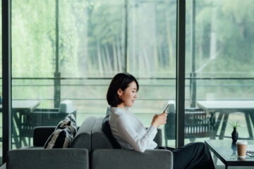 Asian businesswoman texting with smartphone at office window