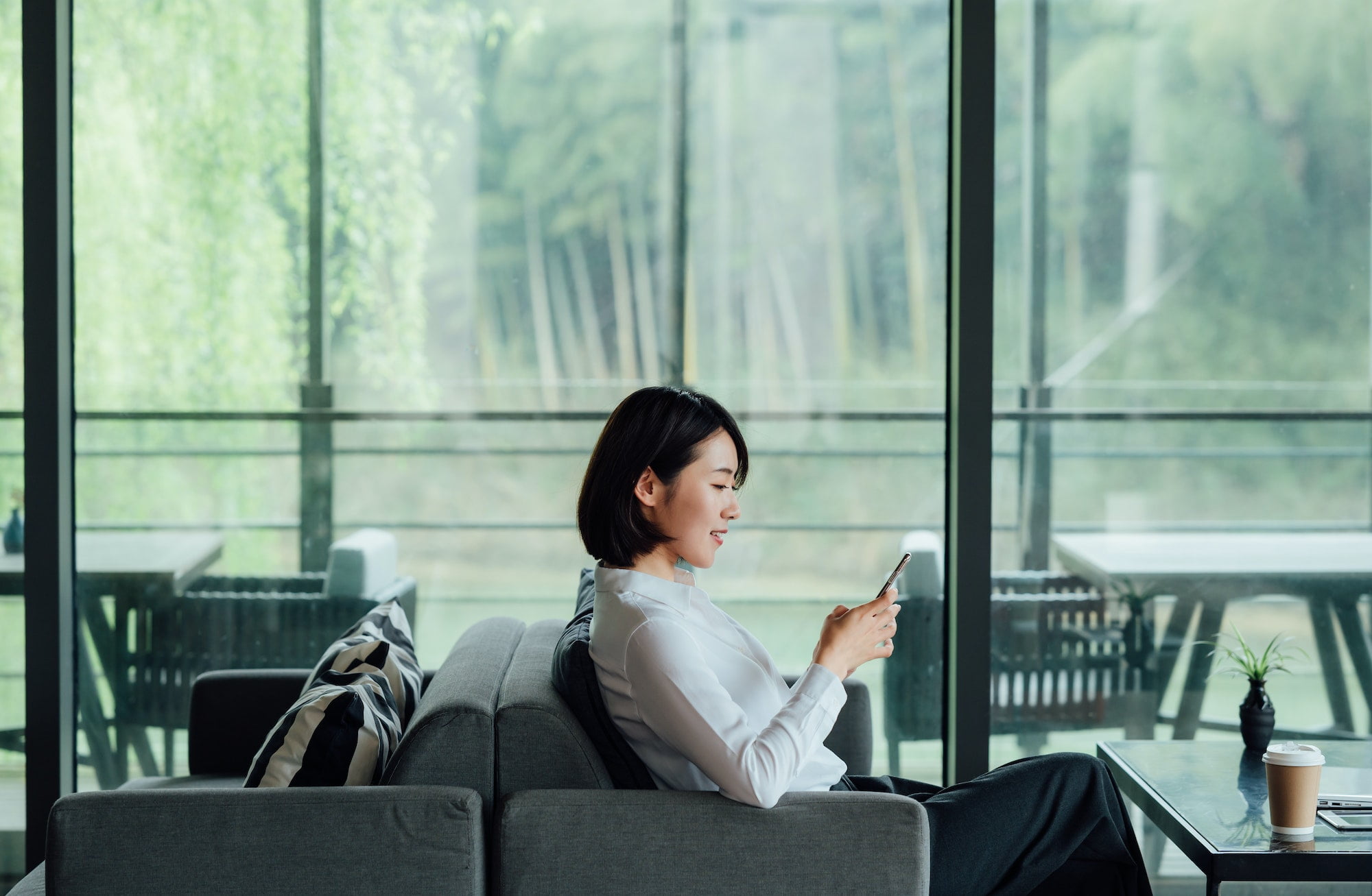 Asian businesswoman texting with smartphone at office window