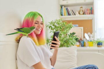 Trendy teen girl with smartphone and quaker parrot on her shoulder