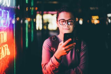 woman looks at phone and walking down street against skyscrapers