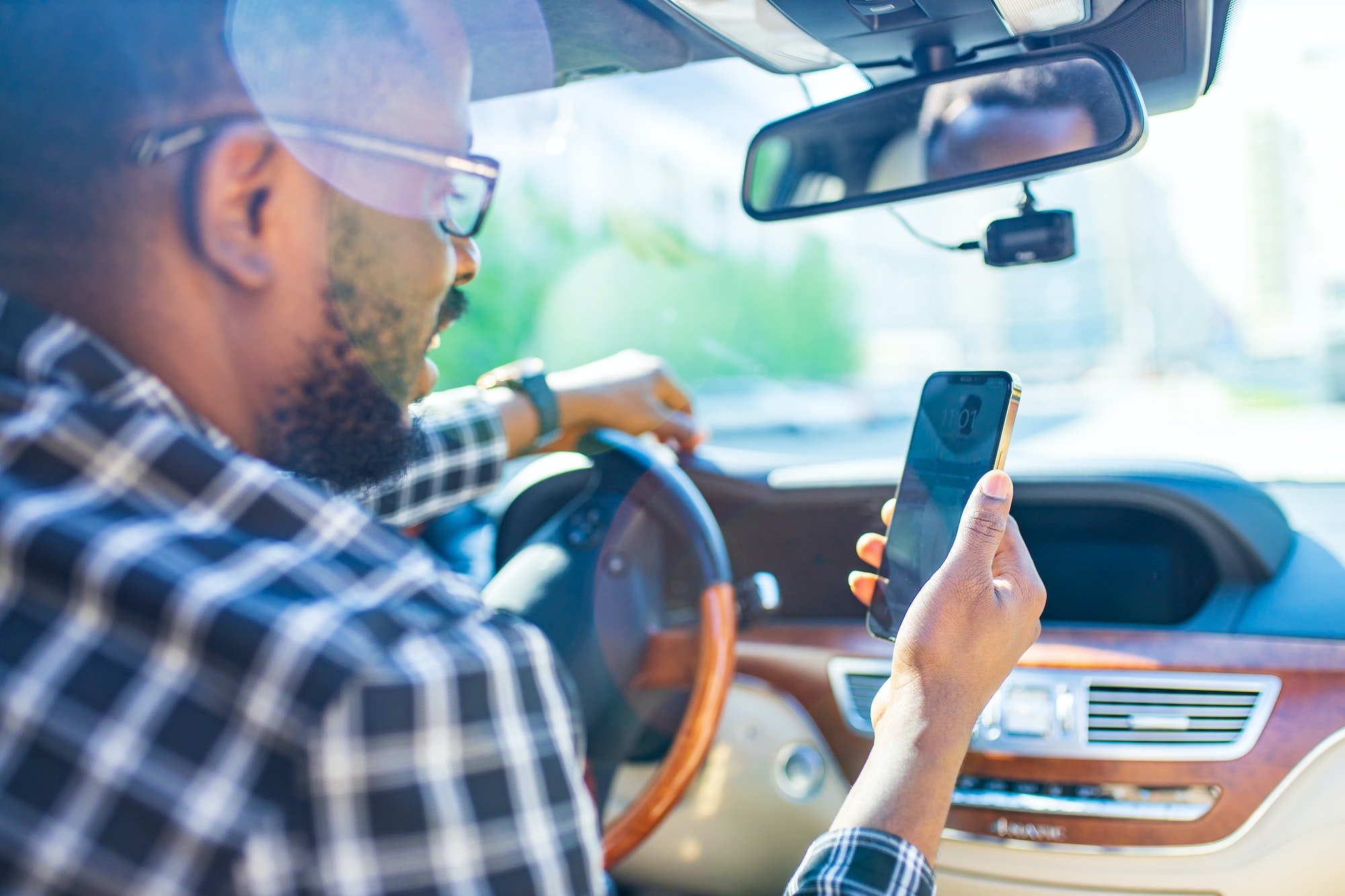 african american man sitting in a car and adjusting rearview mirror looking to phone map app