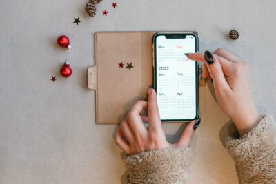 Calendar on the mobile phone with holding hands in a cozy furry sweater and Christmas ornaments.