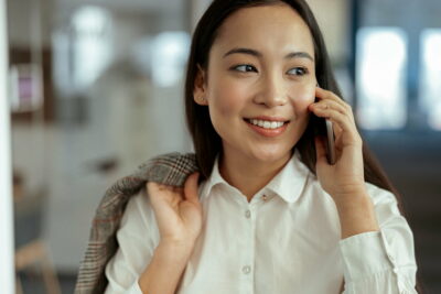 Close up of smiling asian business woman making phone call standing at office