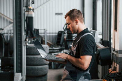 Holding laptop in hands. Man in uniform is working in the auto service