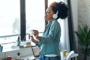 Motivated young afro woman listening to music while dancing in living room at home.