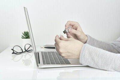 Person opening usb flash next to laptop, Office Work concept on white wall background