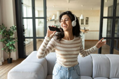 Pretty Caucasian woman in wireless headphones using new music application on smartphone, singing