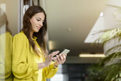 Young businesswoman using smartphone touchscreen in office atrium