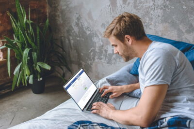 young man in bed using laptop with facebook on screen