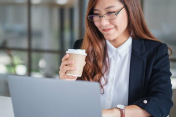 A businesswoman using and typing on laptop while working and drinking coffee in office