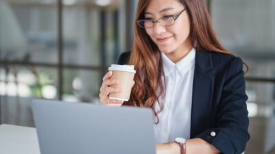 A businesswoman using and typing on laptop while working and drinking coffee in office