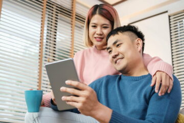 Asian couple watching video live on tablet on sofa in living room