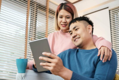 Asian couple watching video live on tablet on sofa in living room