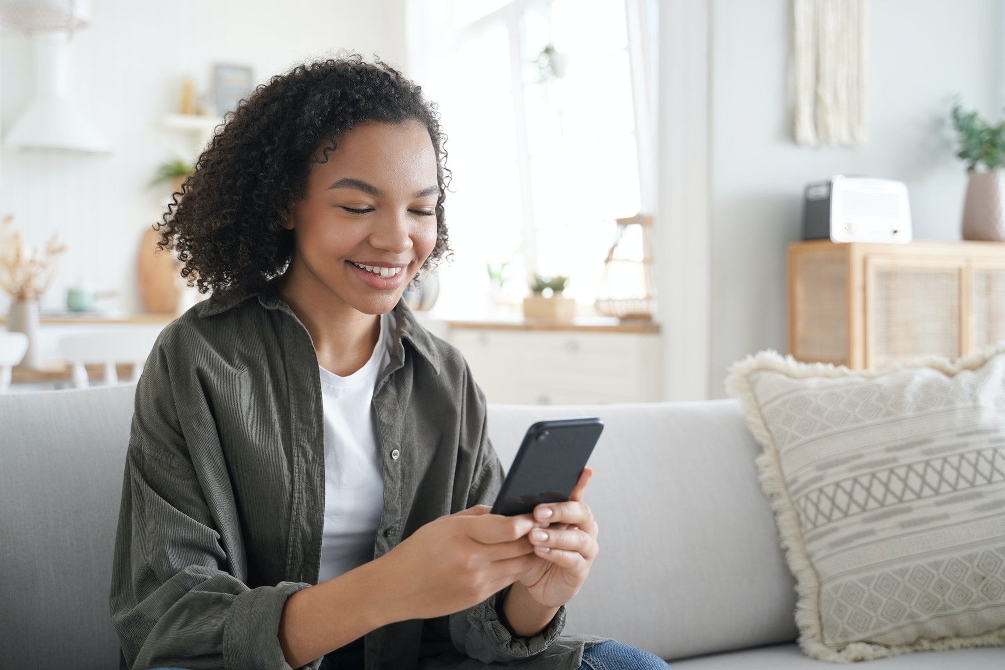 Curly african american girl has fun with phone at home and smiling. Communication concept.