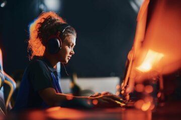 Side view of a young mixed race girl, female cybersport gamer wearing headphones playing online