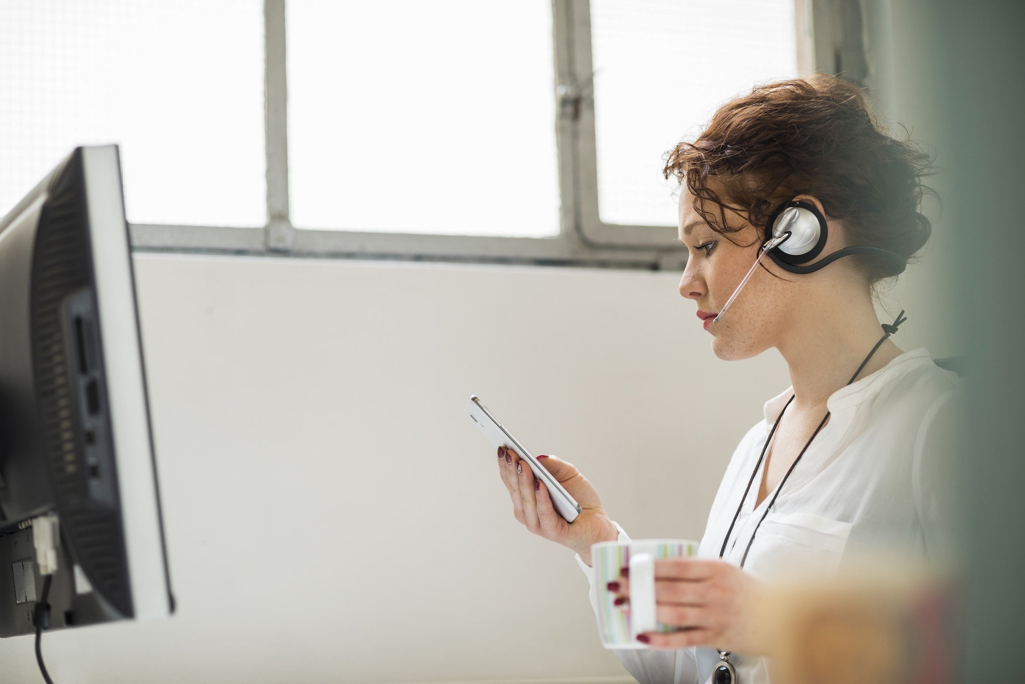 Young woman in office with headset and cell phone