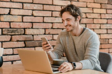 25s smiling attractive businessman working on his laptop and phone in loft cafeteria