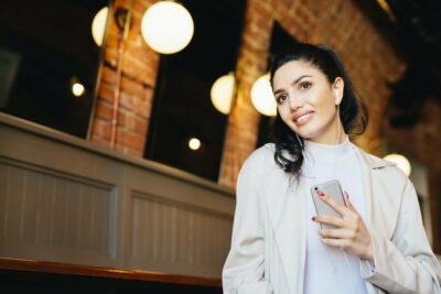 Caucasian beautiful woman holding mobile phone in hand listening to music with earphones