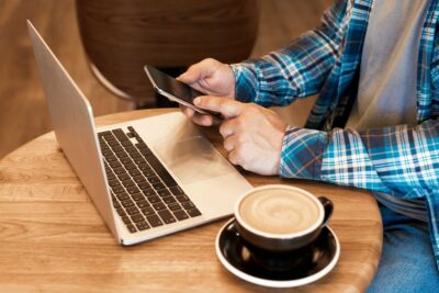 Man freelancer working online with macbook and mobile phone and drinking morning coffee in cafe