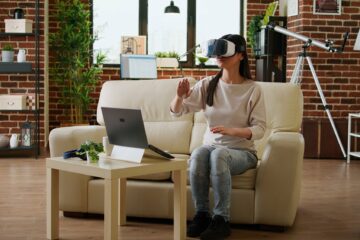 Playful woman with VR goggles playing on metaverse inside living room