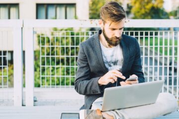 Young bearded businessman using computer and smartphone