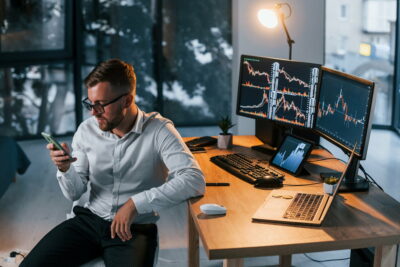 Working at evening time. Young businessman in formal clothes is in office with multiple screens