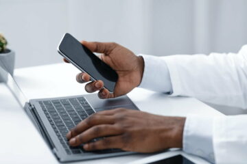 Close up of doc hands holding phone and using laptop