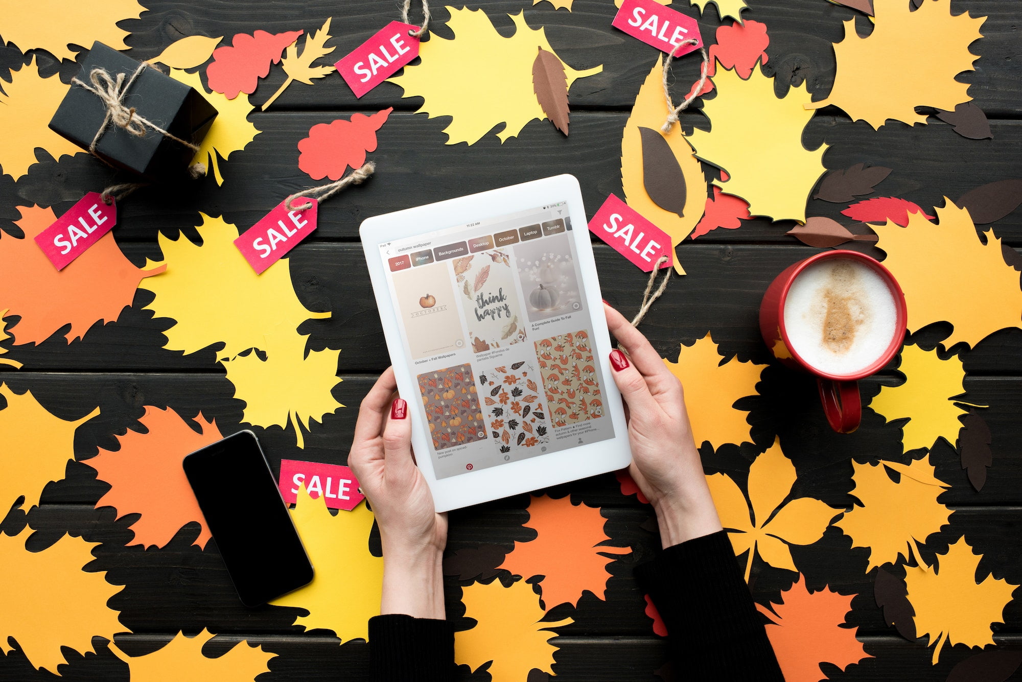 cropped view of female hands with digital tablet with pinterest website on table with autumn leaves,